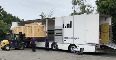Een grote houten kist wordt met heftruck uit een vrachtwagen gehaald.