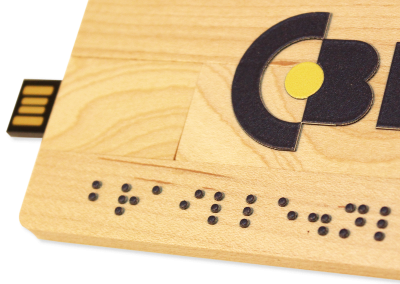 A USB stick made of wood the size of a bank card. A relief image of the CBB logo is printed on the wood. Below the logo 'braille.nl' is printed in braille.
