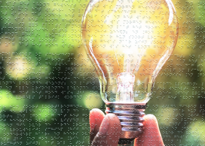 A hand holds up a light bulb. The entire image is covered in a braille text that is illegible if you can't read braille. The purpose of this art object is to raise awareness that reading is not always self-evident.